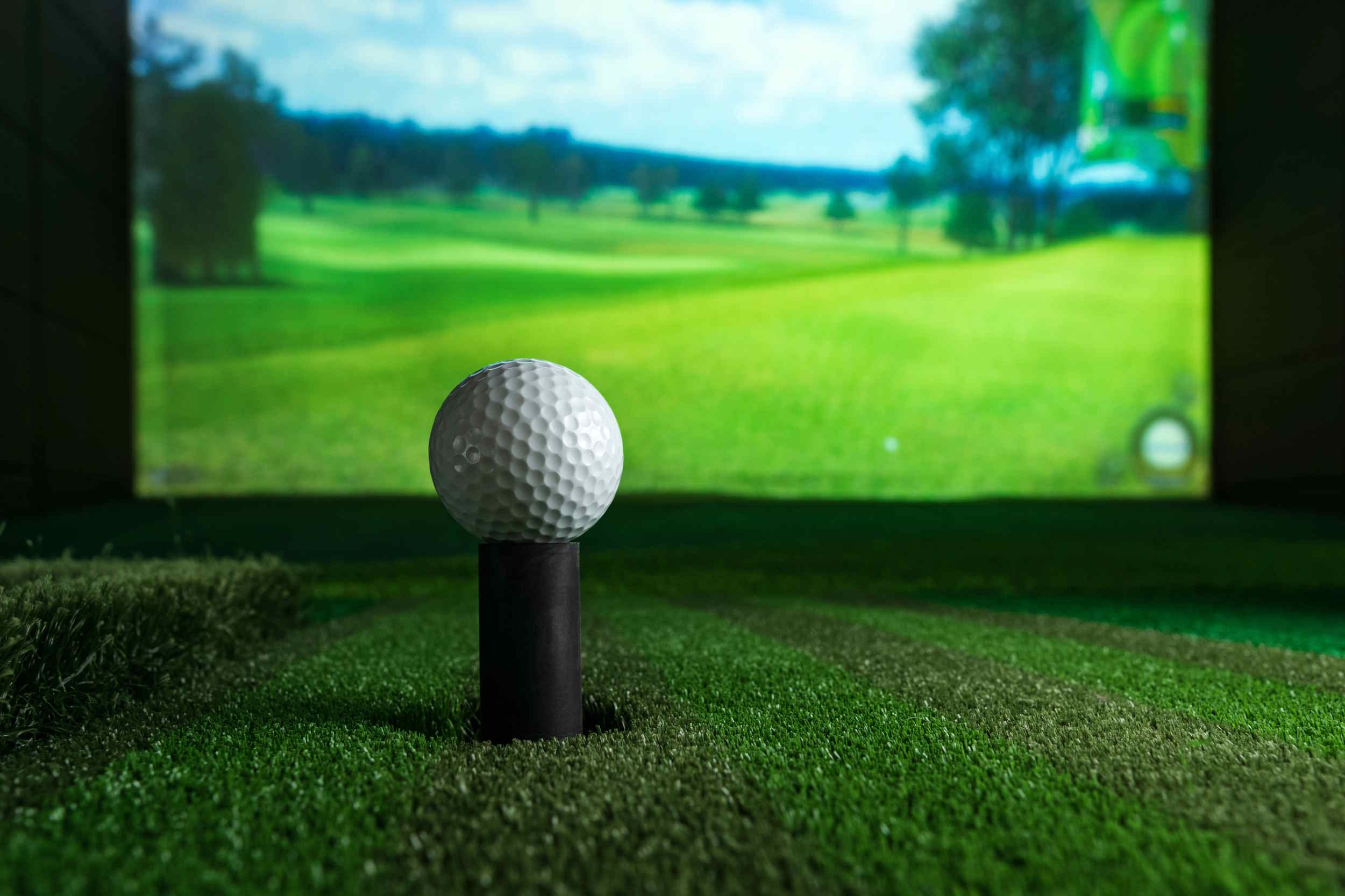 Golf ball on a tee in front of an indoor golf simulator screen