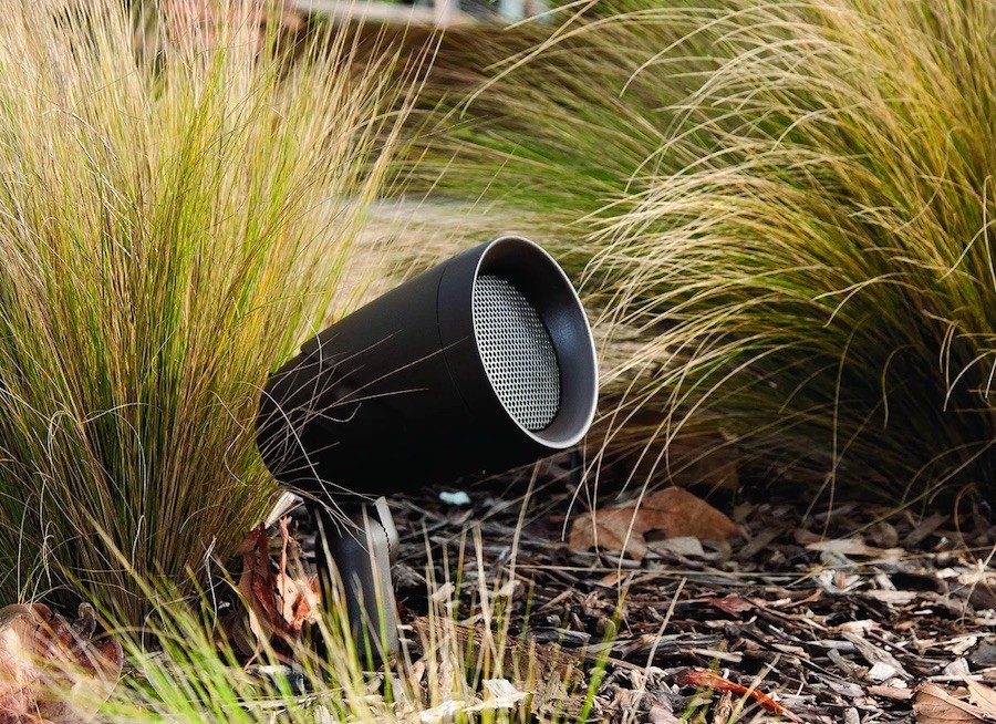 large bullet speaker hiding among mulch and plants