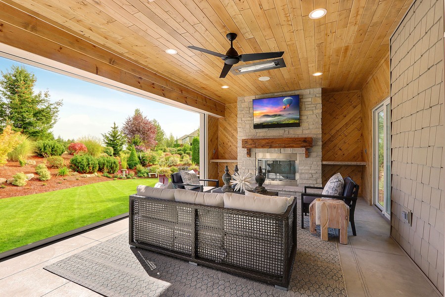 A patio with an outdoor TV, in-ceiling speakers, fan, and a fireplace.