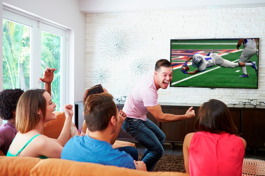 People sitting on a couch watching a football game on a flat-screen TV in a living room