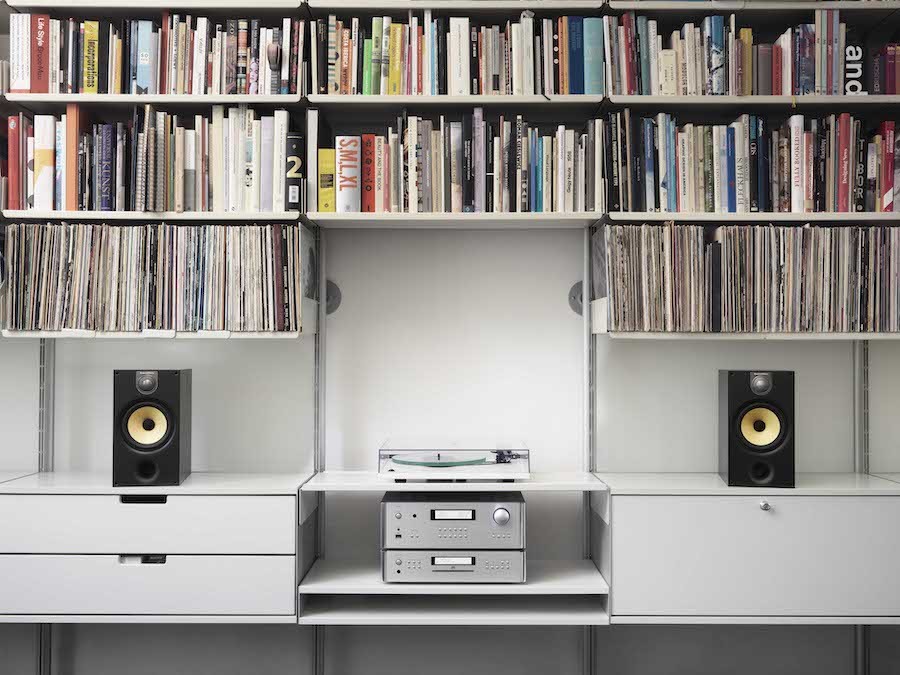 White bookshelves filled with books, records, record player, audio tuner and B&W speakers.