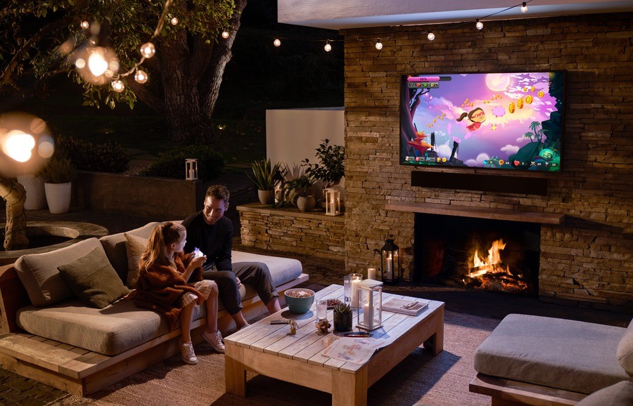A father and daughter on a cozy patio enjoying a cartoon on their outdoor TV.